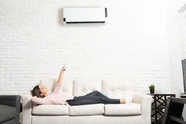 A person relaxes on a sofa, pointing a remote at the sleek mini-split installation adorning the white brick wall.