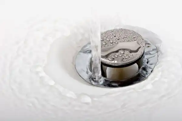 Water flowing into a sink with a metal drain plug coated with water droplets.